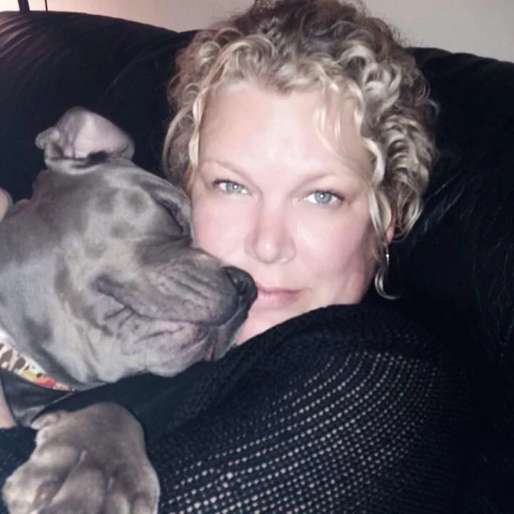 Marcy cuddling her grey dog on a sofa