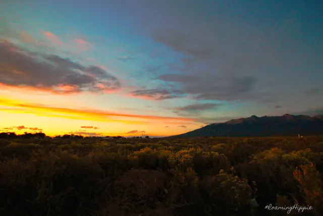 A colourful sunset over dark plains and distant mountains