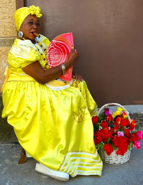 A woman in a bright yellow dress holding a fan, with a basket of flowers