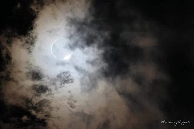 The eclipsed sun peeking through dark clouds