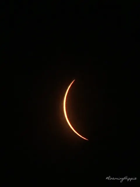 A thin orange crescent of sun against a black sky