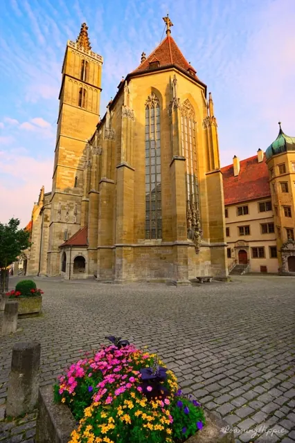 A golden Gothic church above a cobbled square and flowers