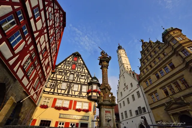 Ornate gabled buildings and a fountain column on a town square