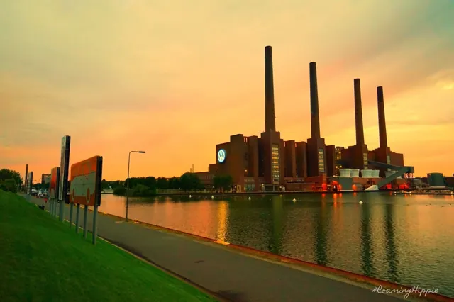 A brick power station with four chimneys reflected in a canal at sunset