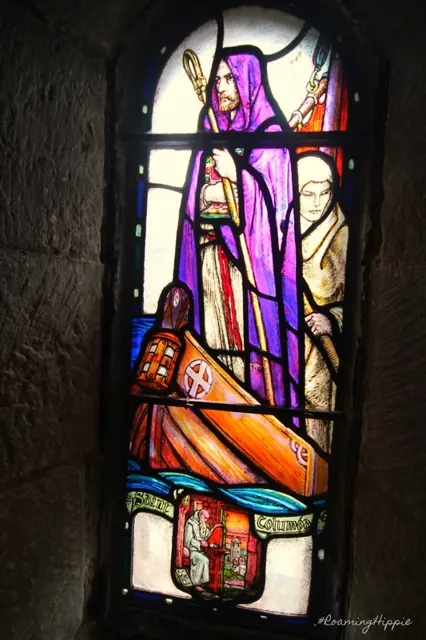 A glowing stained-glass window of a saint in a stone wall