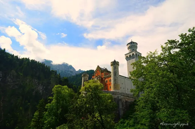 A castle on a forested hill below mountain peaks