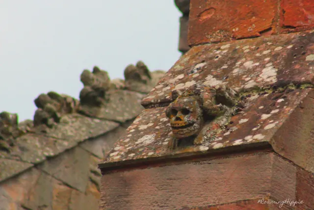Small carved figures along a lichen-covered red stone roofline