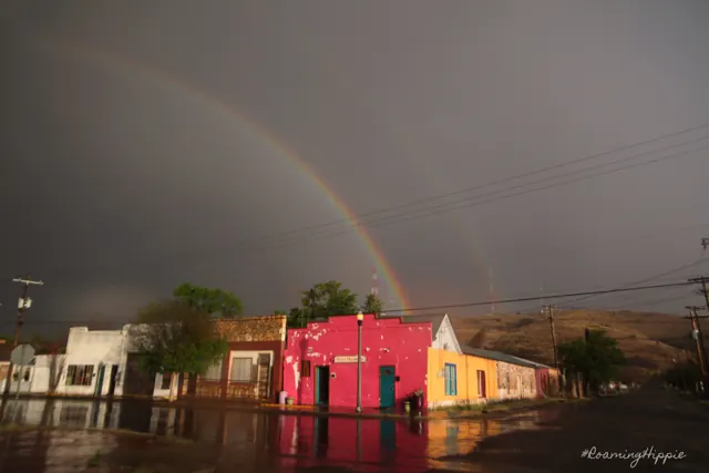 A double rainbow over colourful small-town storefronts after rain