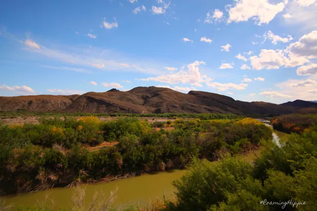 A green river bend below rocky hills and a blue sky
