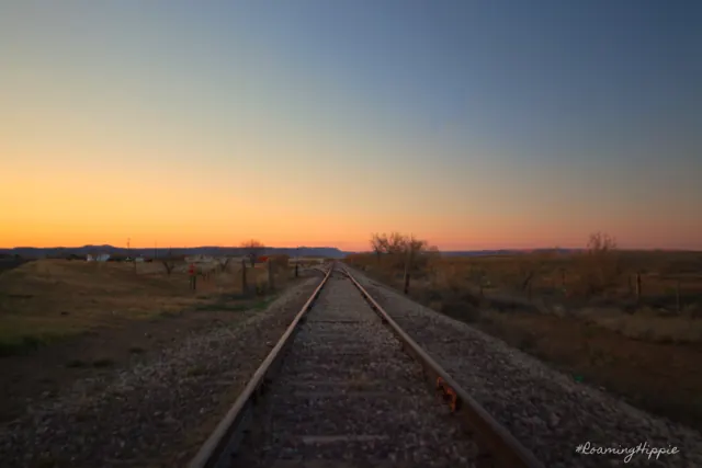 Railroad tracks leading toward a golden sunset horizon