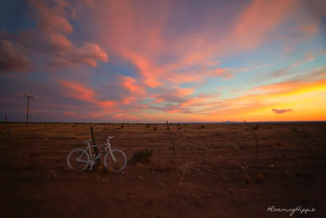 A white bicycle in a field under streaks of pink and orange cloud