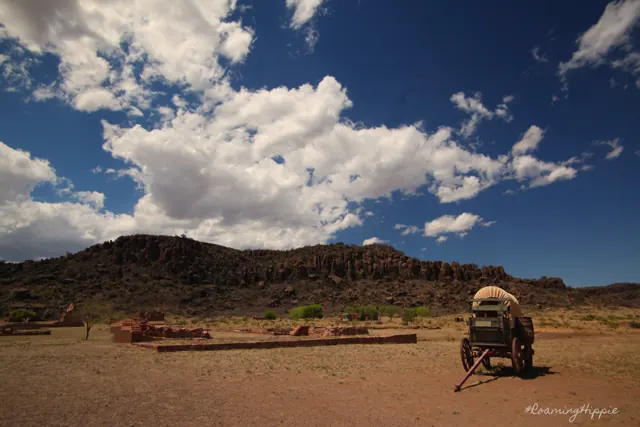 A covered wagon in front of a rocky ridge and white clouds