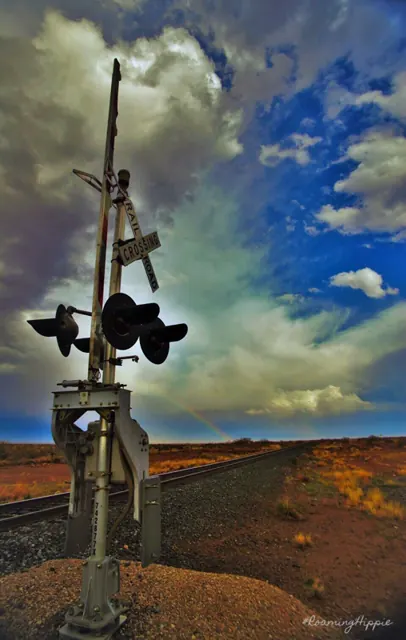 A railroad crossing signal under a dramatic, glowing storm sky