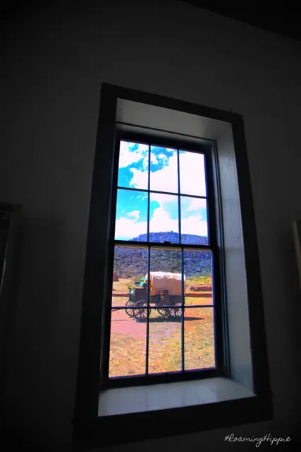 A view through a tall old window to a wagon and hills outside