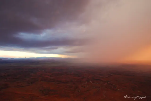 Rain falling from dark clouds over a vast desert canyon